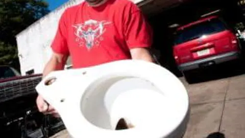 Greg Kohfeldt posa con el inodoro, que tiene unas inscripciones en alemán en su parte inferior