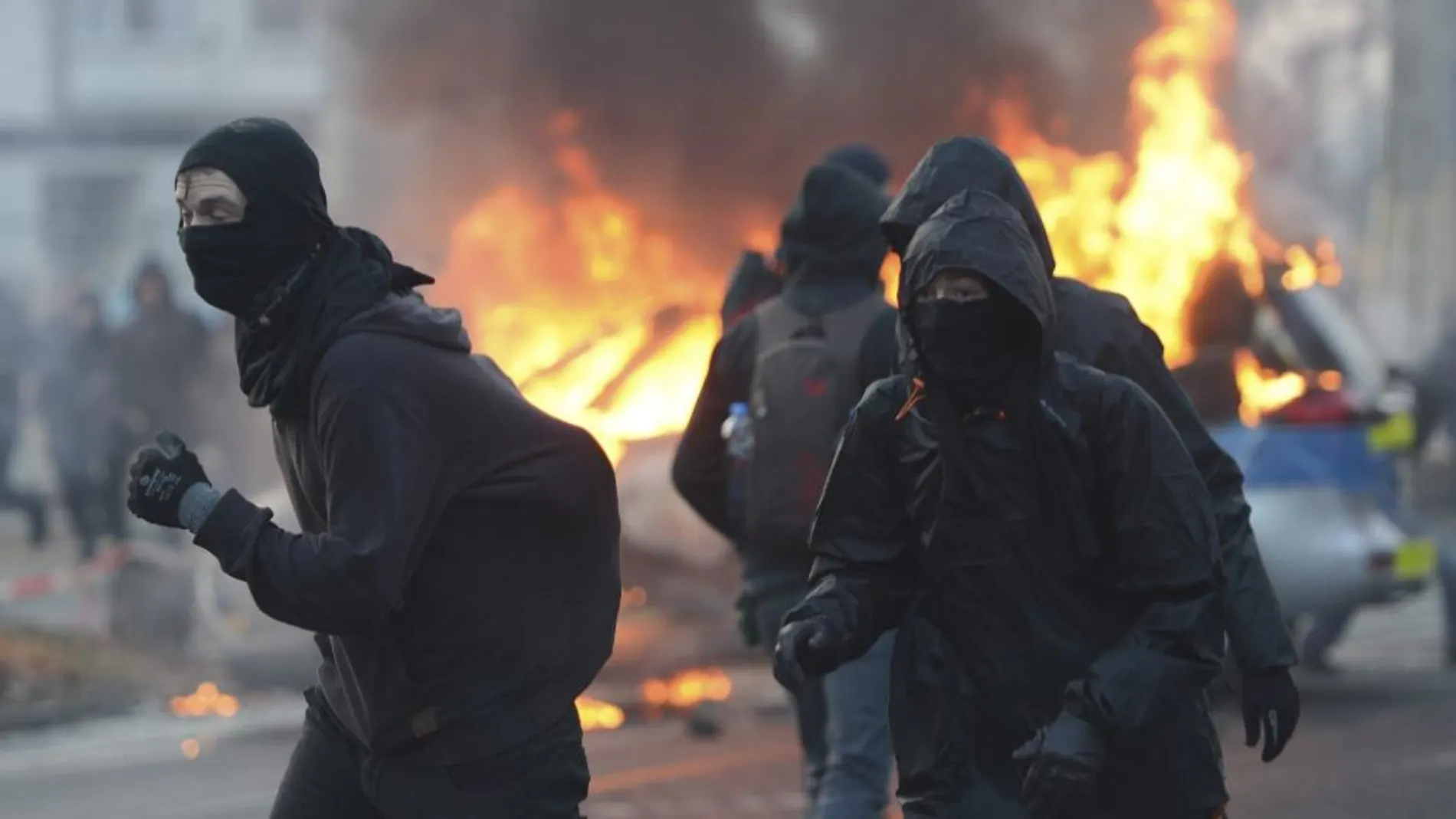 Manifestantes se cubren el rostro junto a un vehículo policial que arde ante la nueva sede del Banco Central Europeo (BCE) en Fráncfort (Alemania).