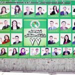 Un hombre se para al lado de un cartel electoral con varios candidatos