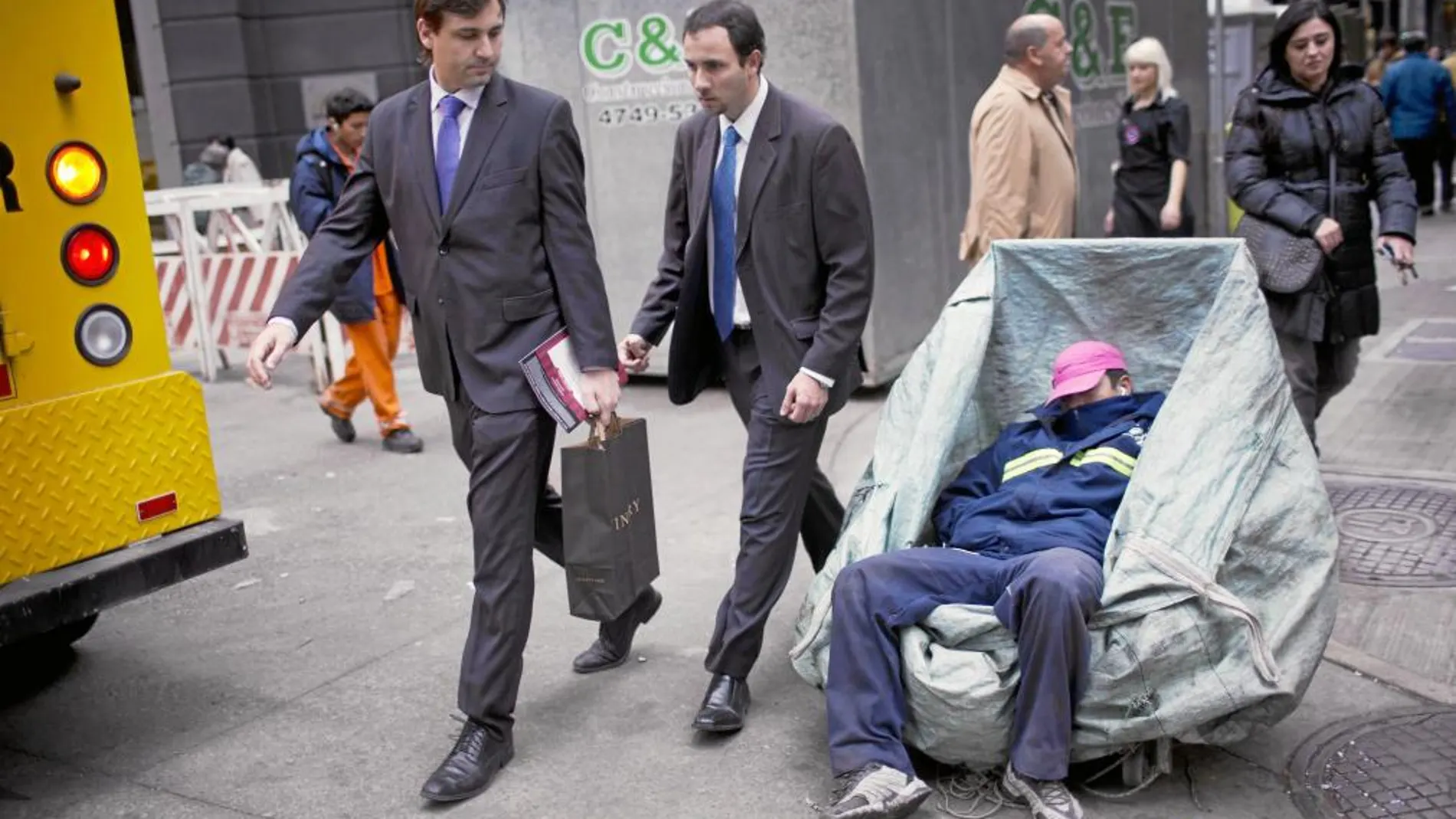 EMPOBRECIMIENTO. Dos oficinistas pasan al lado de un «sin techo» que recicla cartones para vivir en el distrito financiero de Buenos Aires