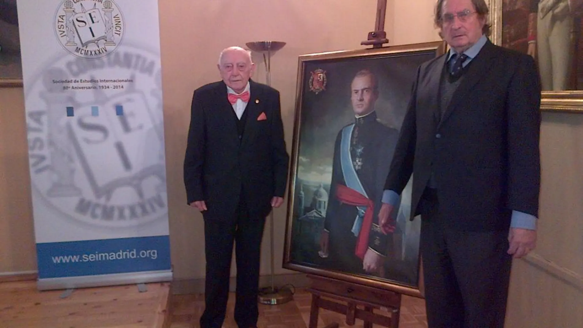 De izda. a dcha. Fernando De Salas López, posando después de su conferencia, junto al óleo de SM el Rey, con Joaquín Antuña, presidente de Paz y Cooperación.