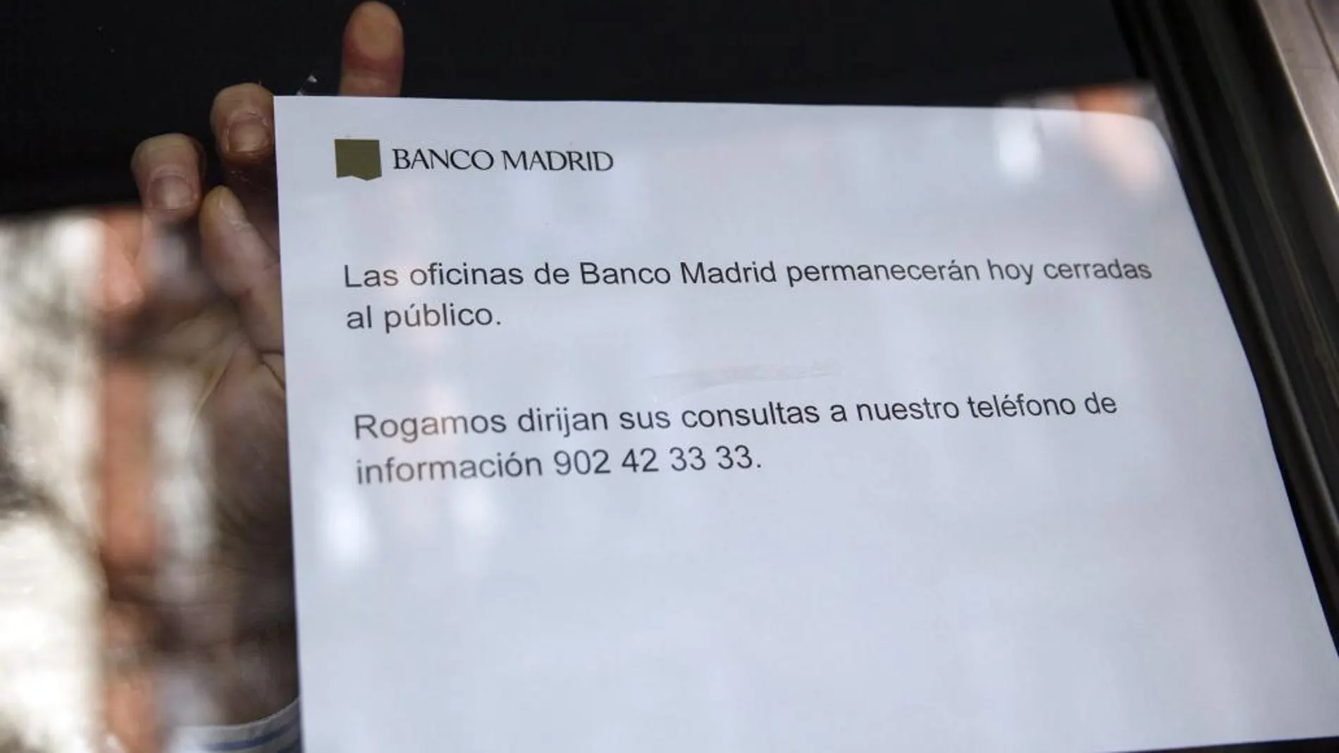 Un empleado coloca un cartel de "cerrado"en una sede del Banco de Madrid