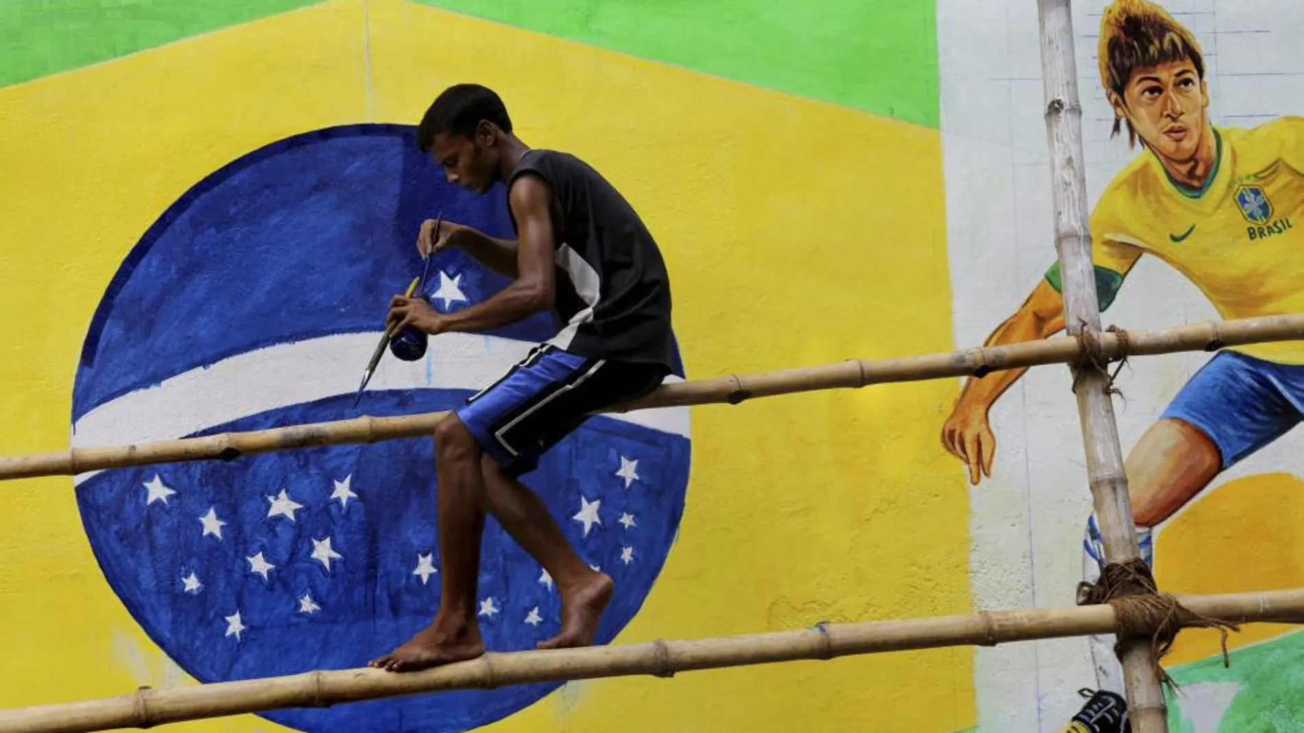 Un artista callejero pinta un mural con la bandera de Brasil y el delantero brasileño Neymar