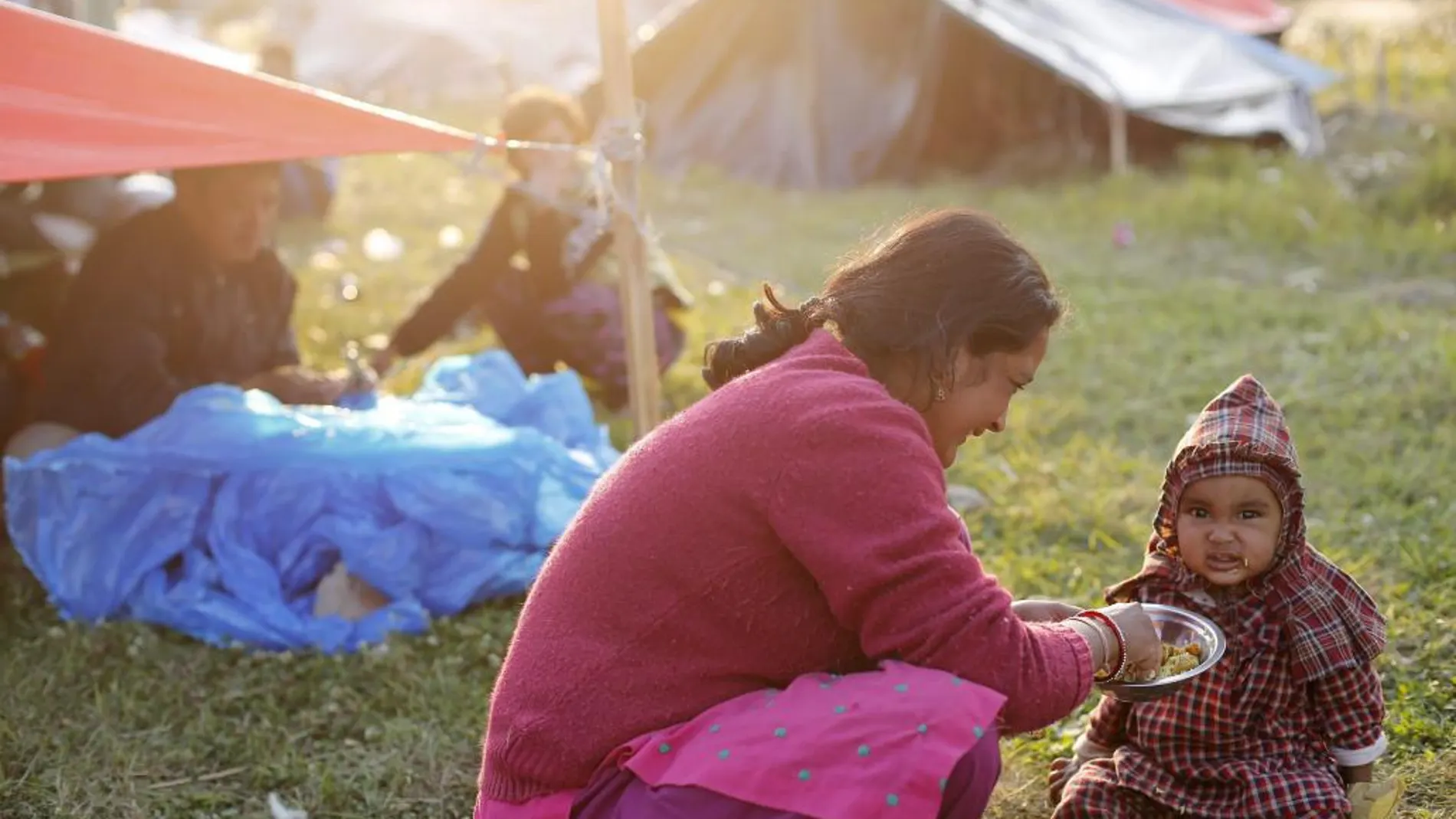 AUna mujer da de comer a su hija en un campamento para los desplazados