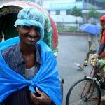 Un conductor de rickshaw de Bangladesh sonríe bajo la lluvia mientras espera la llegada de clientes en una calle de Dacca, Bangladesh