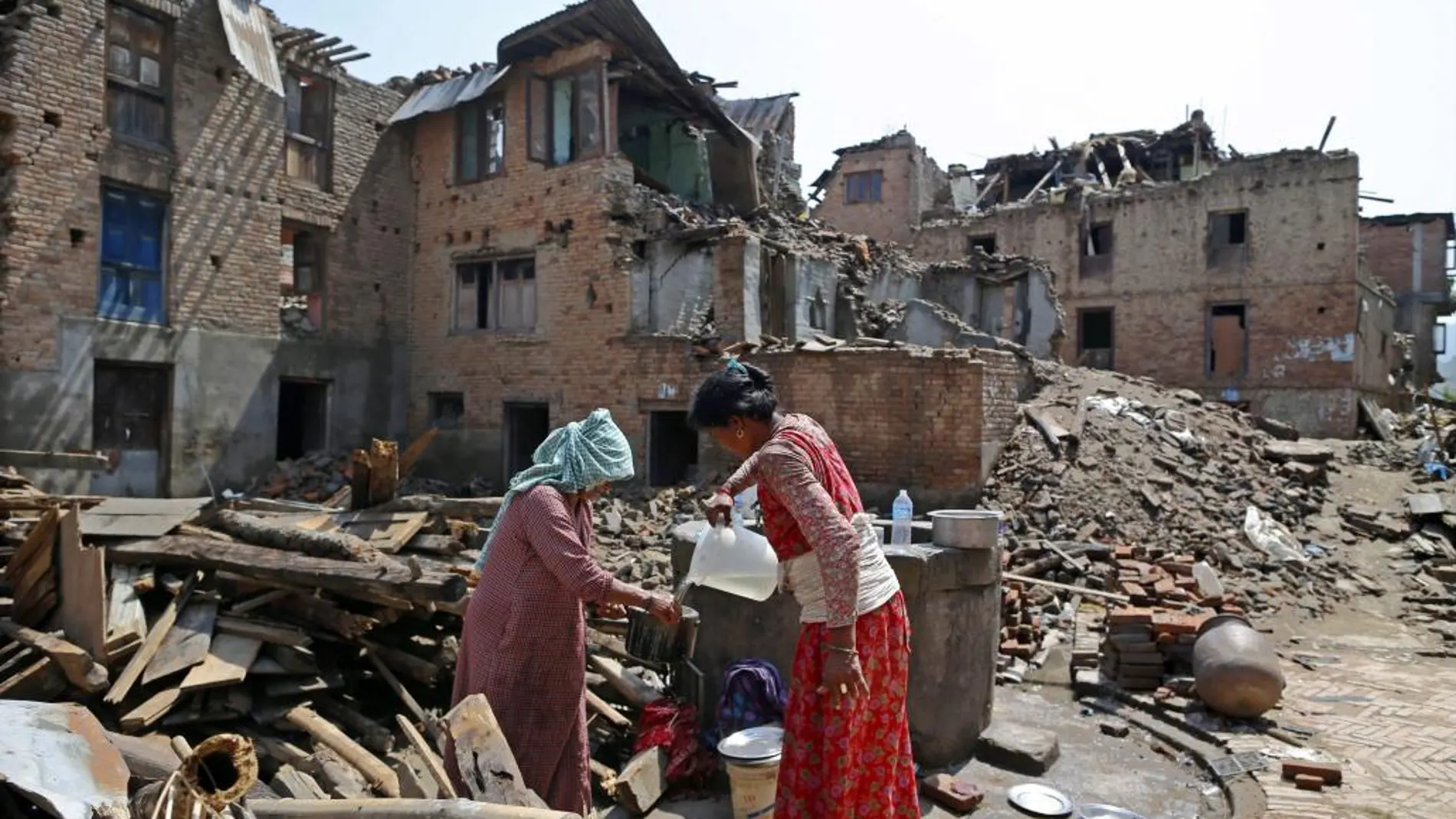 Supervivientes llenan recipientes con agua de un pozo en una zona arrasada en Sankhu