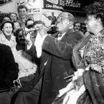 Como un niño, Louis Amstrong, acompañado de su esposa, toca una trompeta de niño a su llegada a Dusseldorf en 1952