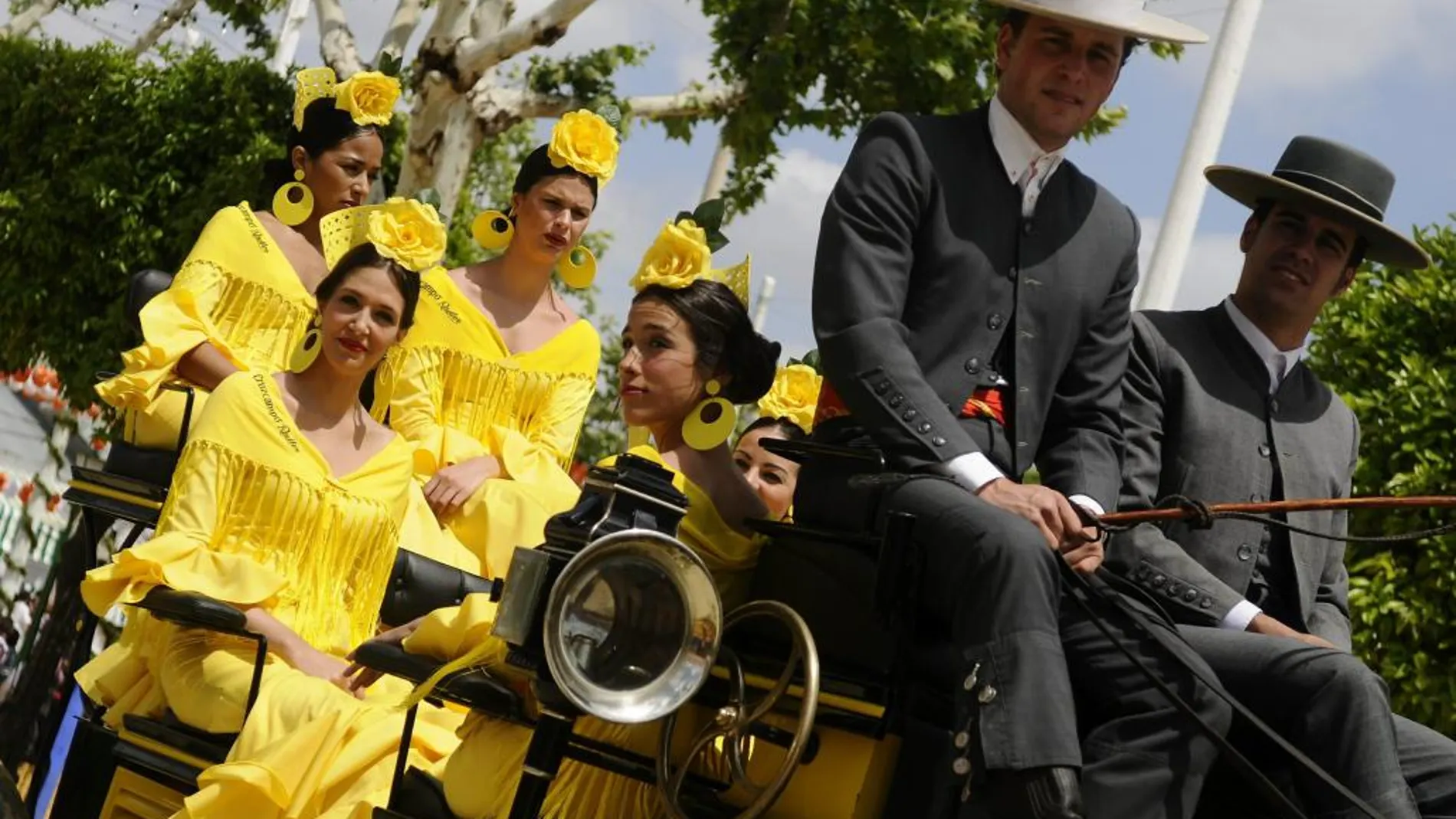 Un coche de caballos con jóvenes vestidas de flamenca pasean por la Feria de Abril