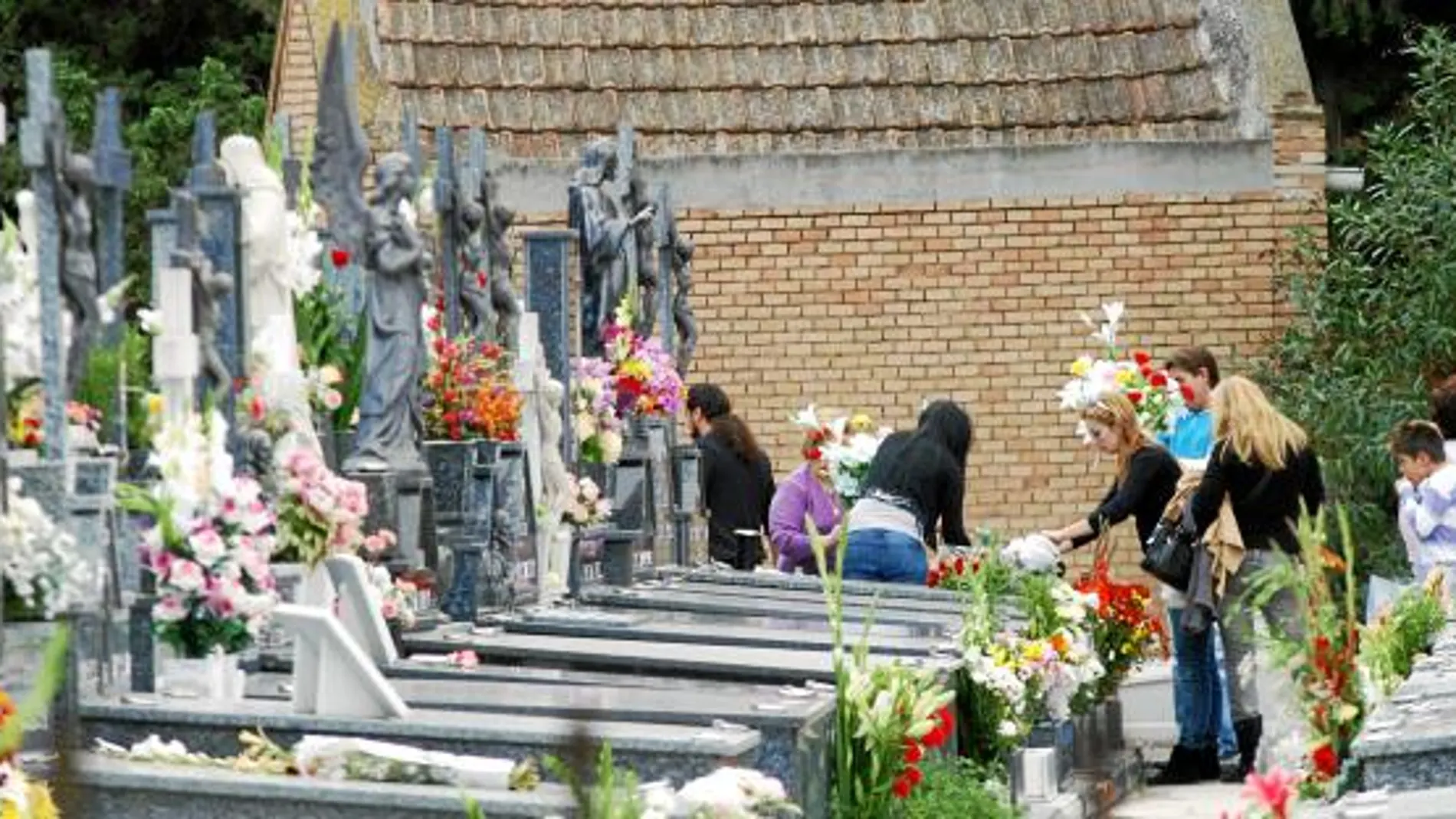 Una familia al completo, colocando varios ramos de flores junto a la tumba de un allegado en el cementerio de Nuestro Padre Jesús de Espinardo