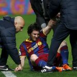 El delantero argentino del FC Barcelona Lionel Messi (c) recibe asistencia médica tras chocar con el portero del Sevilla CF Javi Varas