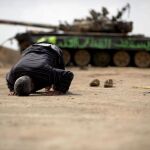 Un insurgente libio reza junto a los restos de un tanque destruído en las proximidades de Ajdabiya, Libia