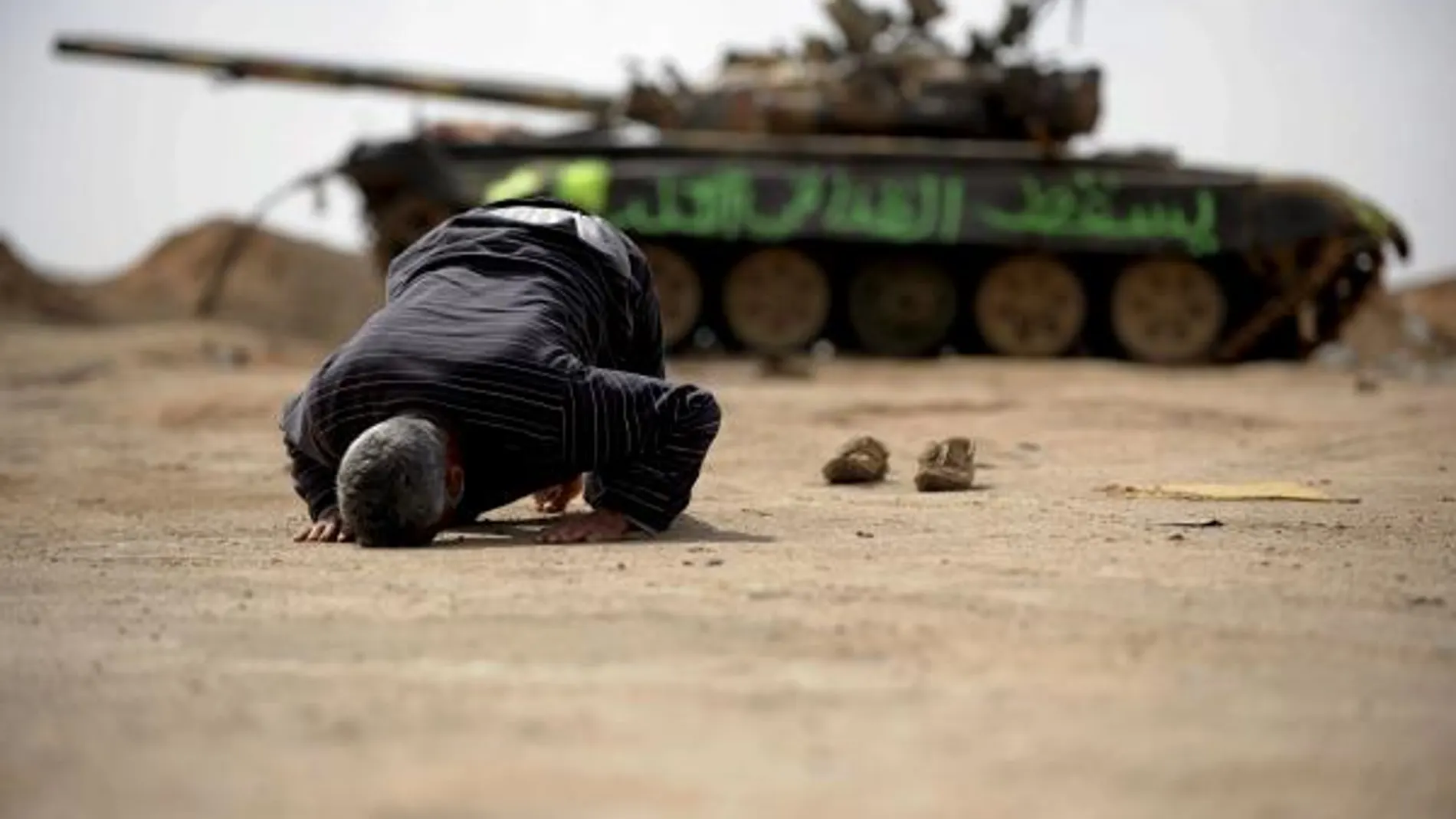 Un insurgente libio reza junto a los restos de un tanque destruído en las proximidades de Ajdabiya, Libia