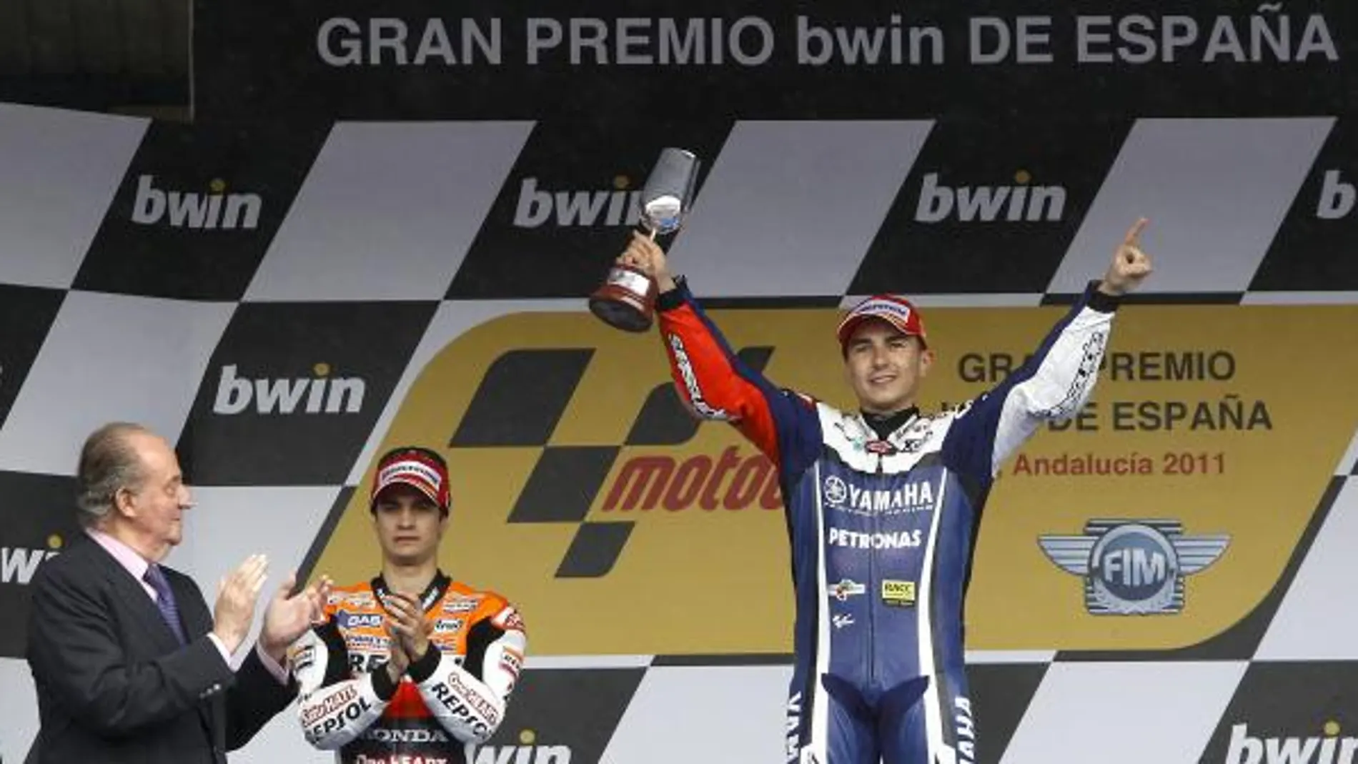 El rey Juan Carlos aplaude al piloto de MotoGP Jorge Lorenzo que celebra en el podio la victoria conseguida en el Gran Premio de España de su categoría, junto al segundo clasificado, Dani Pedrosa