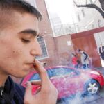 Un joven fuma un cigarrillo en la puerta de su colegio y frente a una escuela infantil