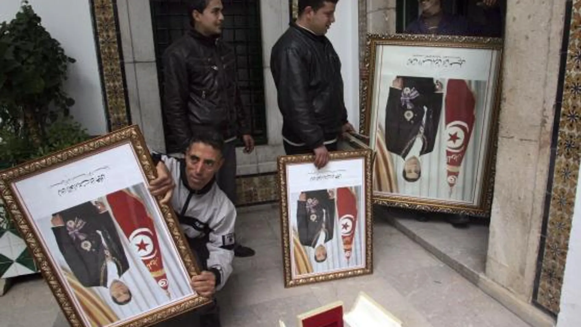 Varios operarios se llevan retratos del huído presidente tunecino, Zine el Abidine Ben Alí, que decoraban uno de los edificios de la sede del primer ministro, al sótano del edificio en Túnez (Túnez)
