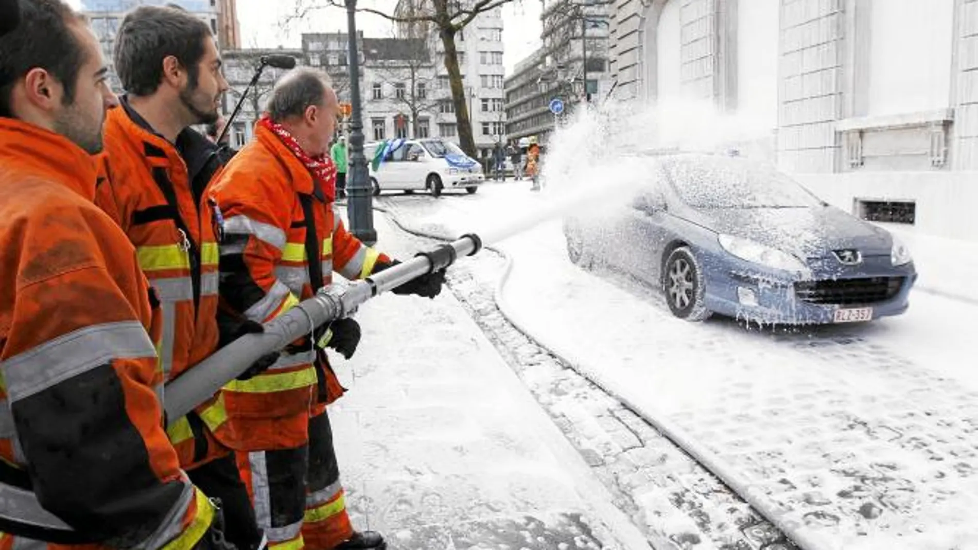 Un grupo de bomberos rocía con espuma un coche durante la jornada de huelga, ayer en Bruselas