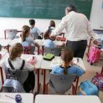 Un profesor se acerca a una alumna para explicarla la materia ante la atenta mirada de sus compañeras y la presencia del crucifijo en el aula