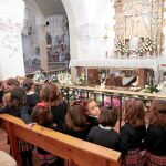 Una fiel muestra una imagen de Santa Ángela; arriba un grupo de niñas le cantan