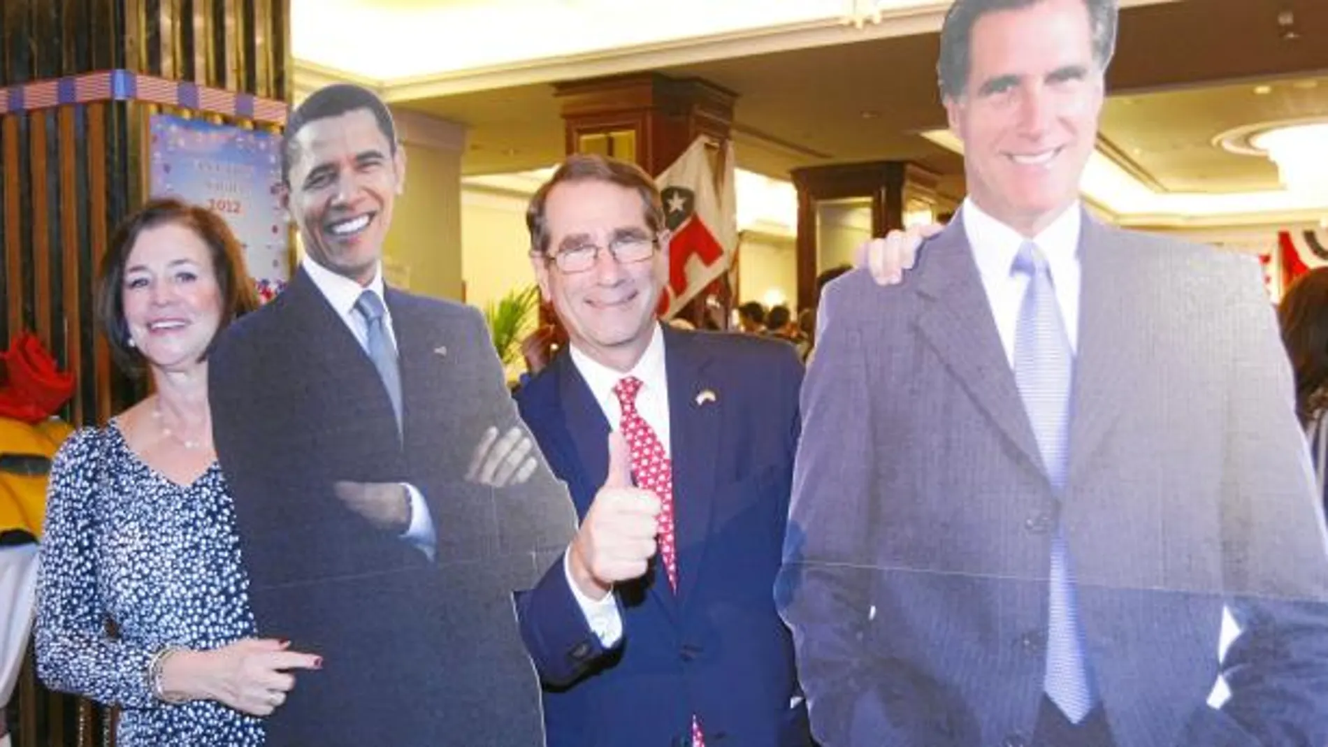 El embajador de EE UU en España, Alan Solomon, posa junto a su mujer, Susan, entre los pósters a tamaño real de los dos candidatos a la presidencia Mitt Romney y Barack Obama.
