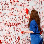 Una mujer pinta de rojo en un mural los nombres de mujeres víctimas de malos tratos