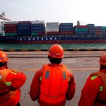 Trabajadores del puerto de Qingdao observan pasar a un barco contenedor de la compañía china Sinotrans Shipping Ltd