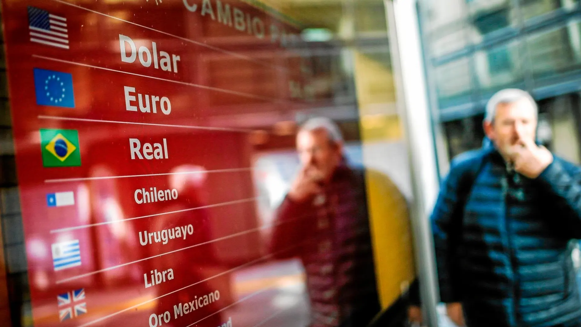Un transeúnte pasea por las calles de Buenos Aires frente a una pantalla con el cambio de divisas