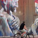 Un ciclista pasa frente a un mural en la última jornada del VII Festival Internacional de Arte Urbano Art Aero Rap de La Bañeza (León)