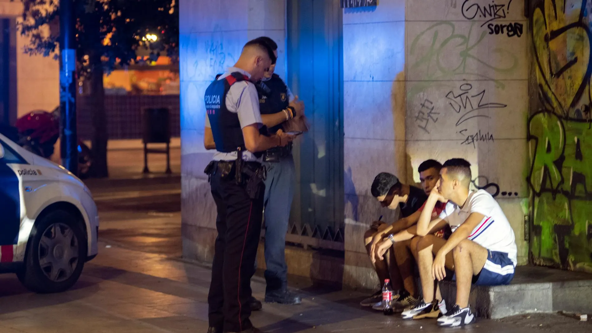 Dos agentes de los Mossos d'Esquadra proceden a identificar a un grupo de jóvenes en Barcelona durante la noche