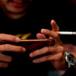 un hombre fuma mientras juega con su teléfono móvil