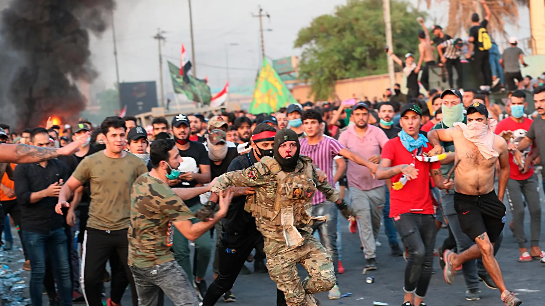 Manifestantes antigubernamentales ayudan a un miembro de las fuerzas de seguridad en una manfiestación en Bagdad/Ap