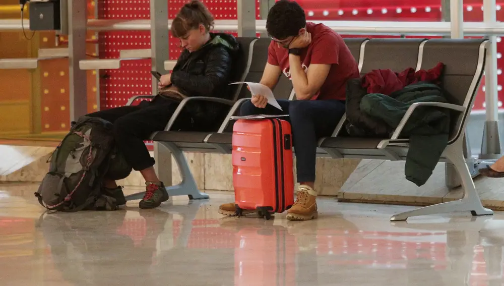 Dos personas esperan su vuelo sentados en un banco del Aeropuerto de Madrid-Barajas Adolfo Suárez | Europa Press