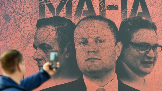 Un hombre hace una foto de un cartel que muestra al primer ministro, Joseph Muscat, su jefe de Gabinete, Keith Schembri, y el ministro de Turismo, Konrad Mizzi