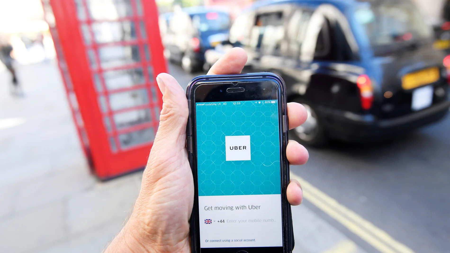 FILE PHOTO: A photo illustration shows a London taxi passing as the Uber app logo is displayed on a mobile telephone, as it is held up for a posed photograph in central London
