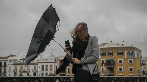 Una racha de viento desbarata el paragüas de una viandante mientras camina por el Puente de Isabel II, en Sevilla (Andalucía)SEVILLA, 22.11.19. Temperaturas. Rachas de viento y lluvia en la capital hispalense.María José López / Europa Press22/11/2019