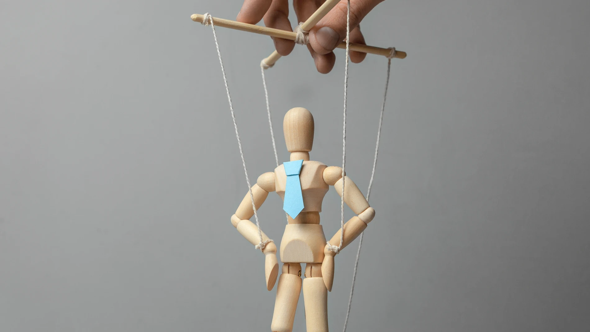Businessman leader in tie on gray background. Deryannaya doll on the threads that pulls the puppeteer. Concept of how to manage staff or leader. puppet