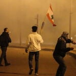 Manifestantes ondean una bandera libanesa mientras uno de ellos lanza un objeto contra la Policía en Beirut