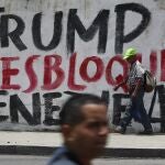 Varias personas pasan en Caracas delante de una pintada pidiendo el desbloqueo de Trump en Venezuela.