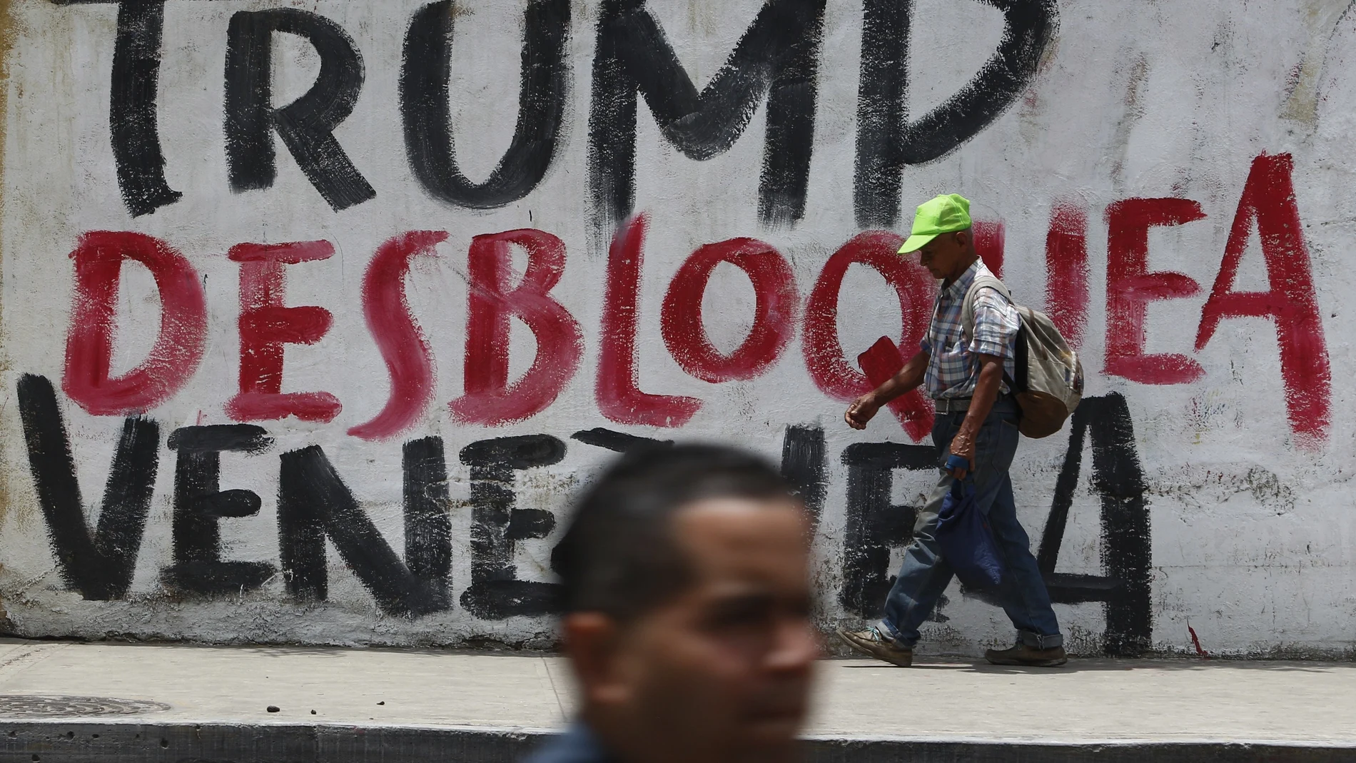 Varias personas pasan en Caracas delante de una pintada pidiendo el desbloqueo de Trump en Venezuela.