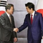 El presidente surcoreano, Moon Jae In, estrecha la mano del primer ministro nipón, Shinzo Abe, en su primer encuentro en 15 meses