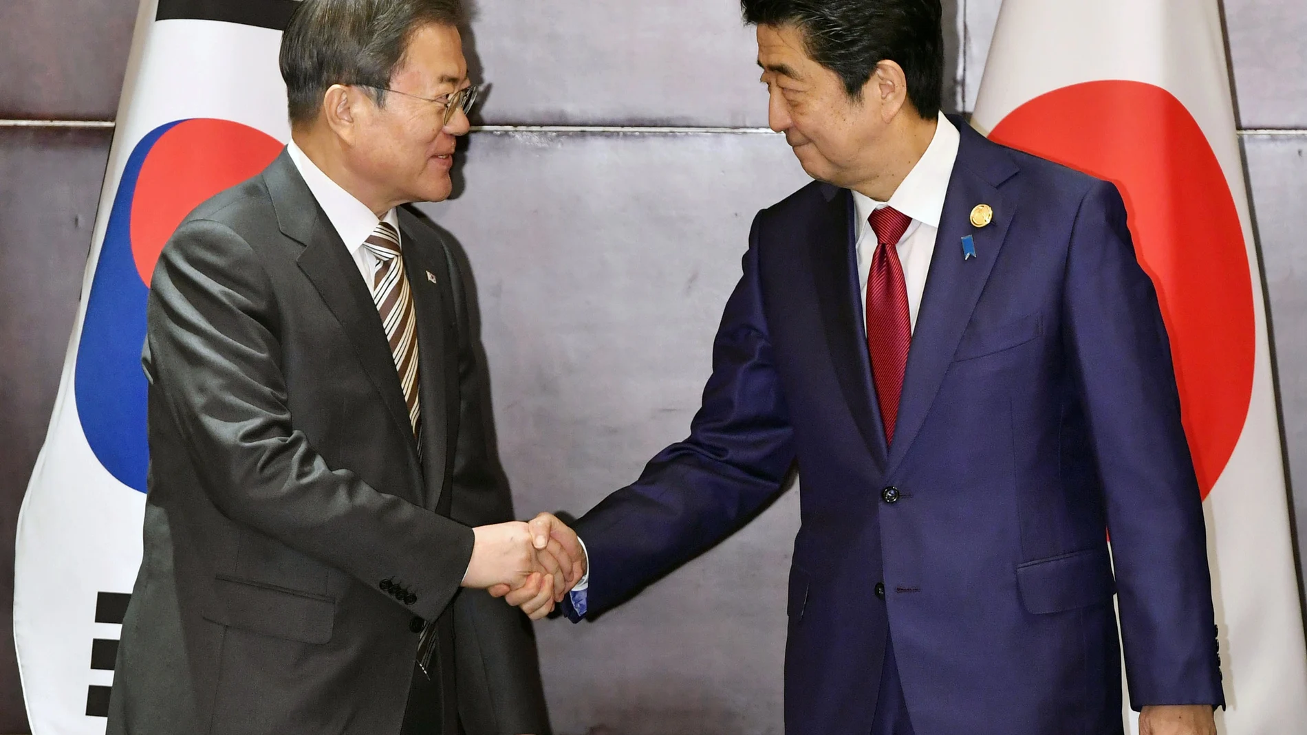 El presidente surcoreano, Moon Jae In, estrecha la mano del primer ministro nipón, Shinzo Abe, en su primer encuentro en 15 meses
