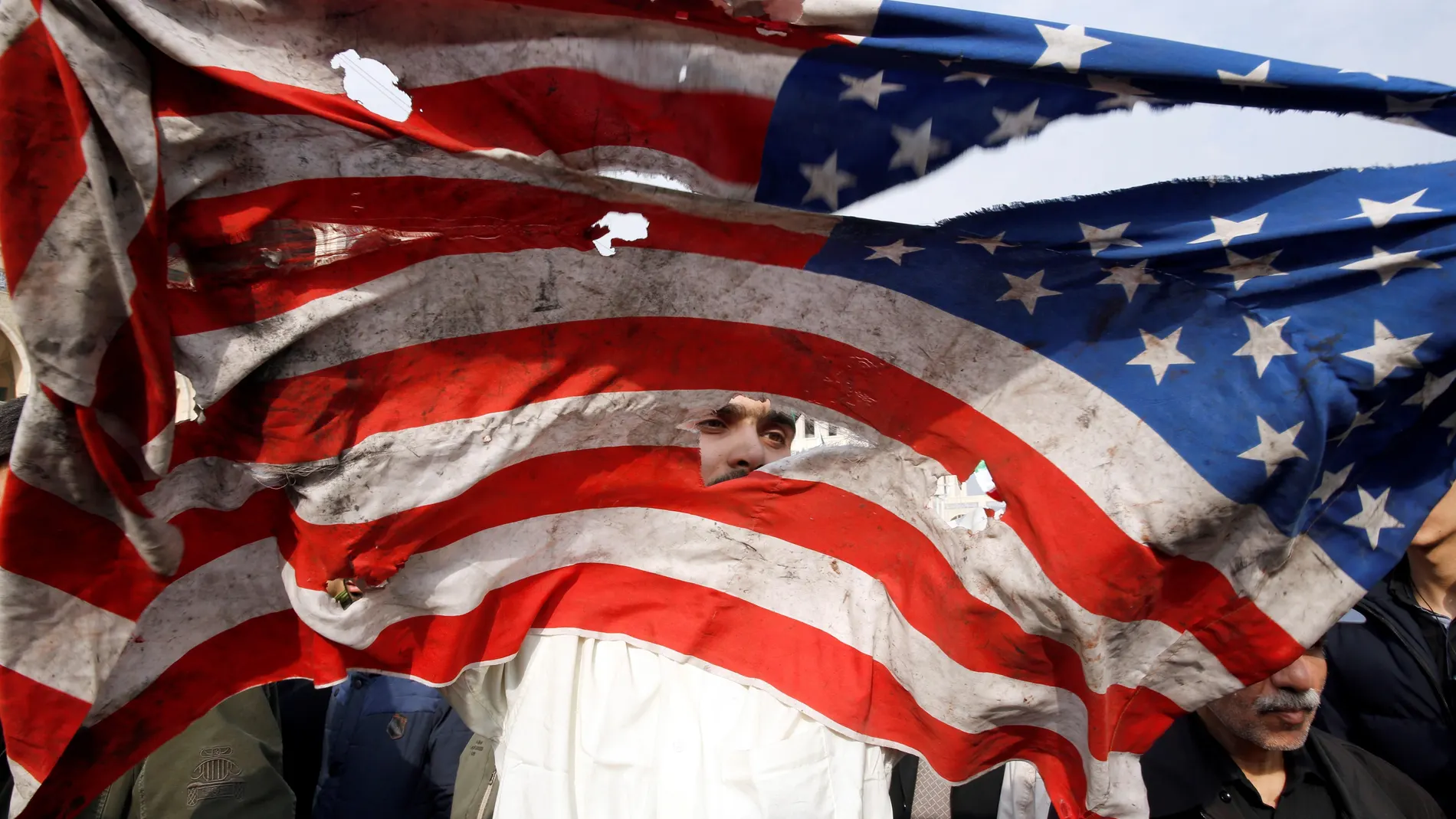 Un manifestante rompe una bandera estadounidense durante una manifestación multitudinaria contra EE UU
