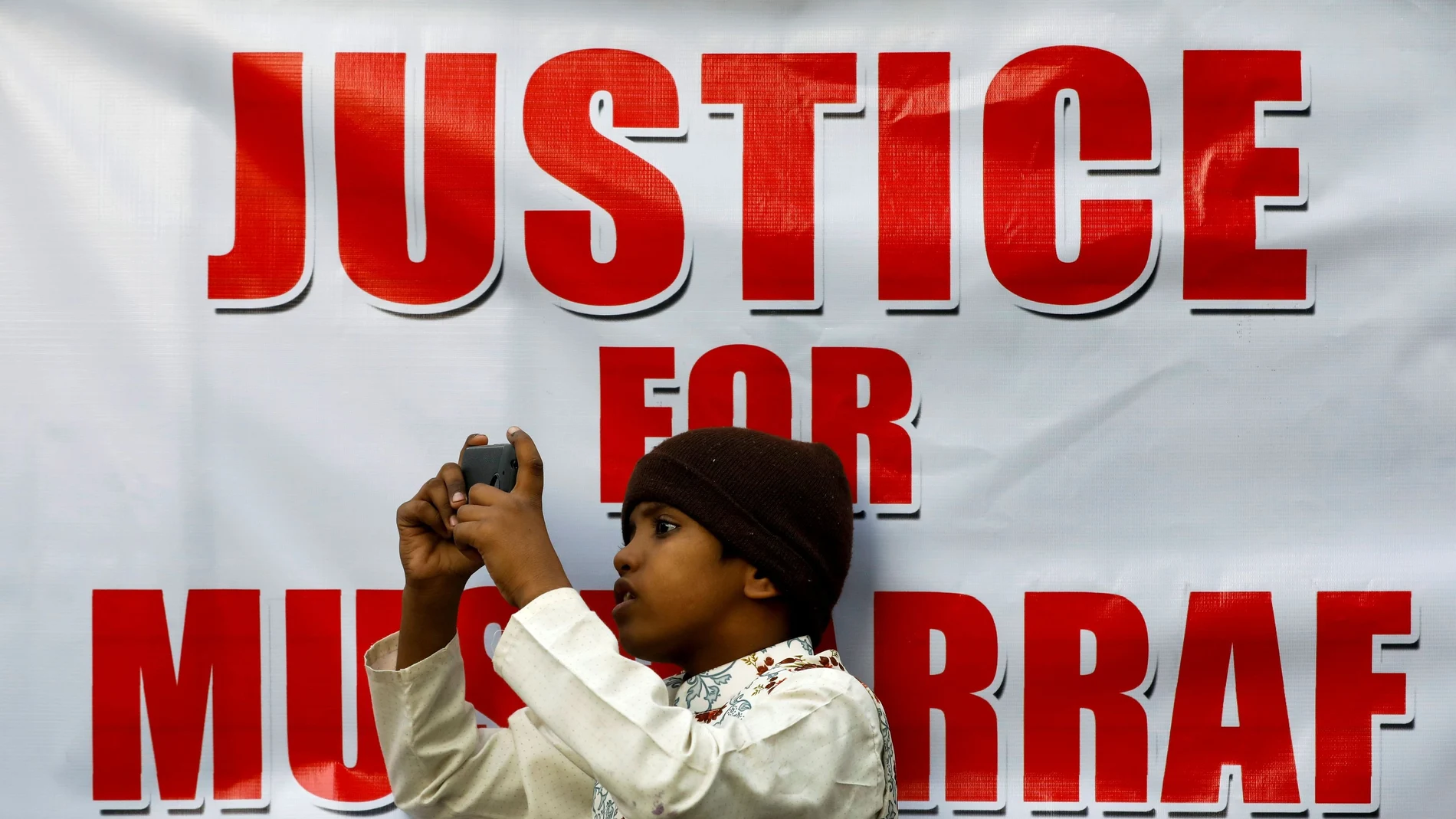 FILE PHOTO: A boy leans on a sign as he films the supporters of Pervez Musharraf, after a Pakistani court sentenced the former military ruler to death on charges of high treason and subverting the constitution, during a protest in Karachi