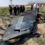 Un grupo de curiosos se congrega junto a los restos del avión ucraniano mientras un técnico busca pruebas del siniestro