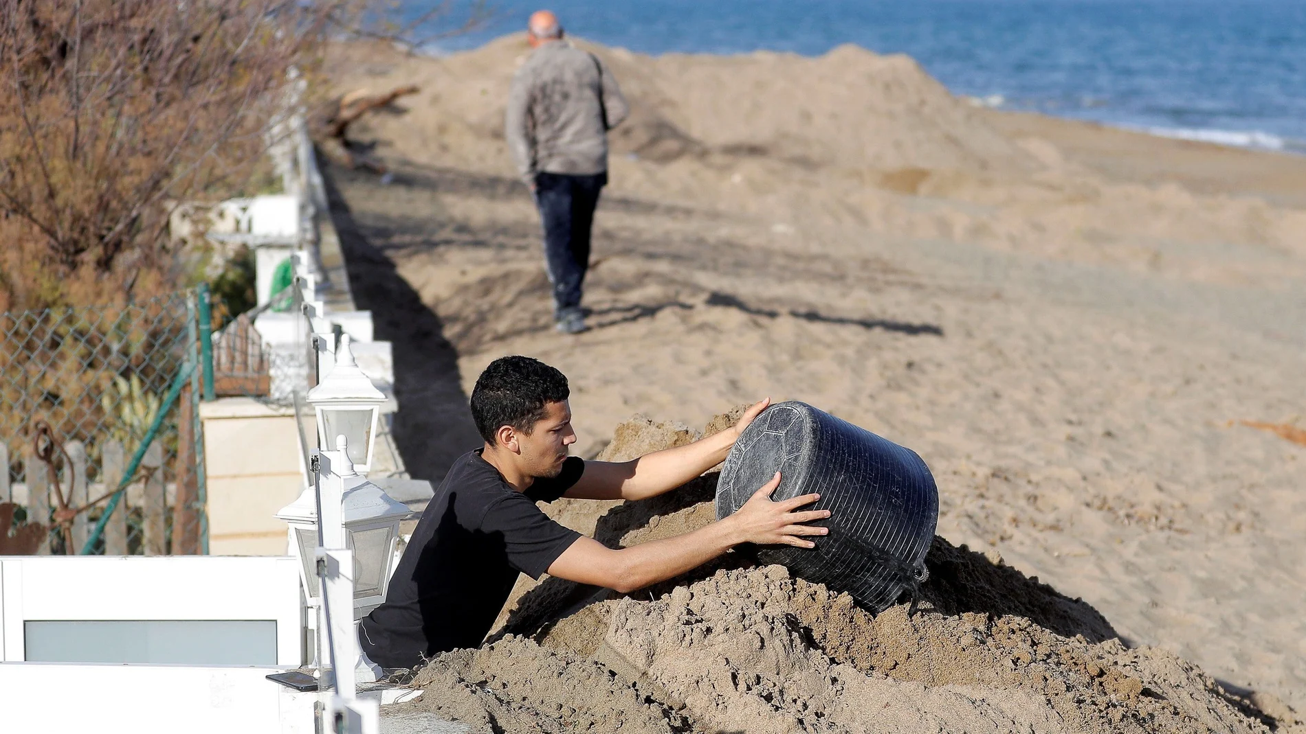 Un hombre retira los cerca de dos metros de arena que el temporal Gloria ha acumulado ante su vivienda de Dénia