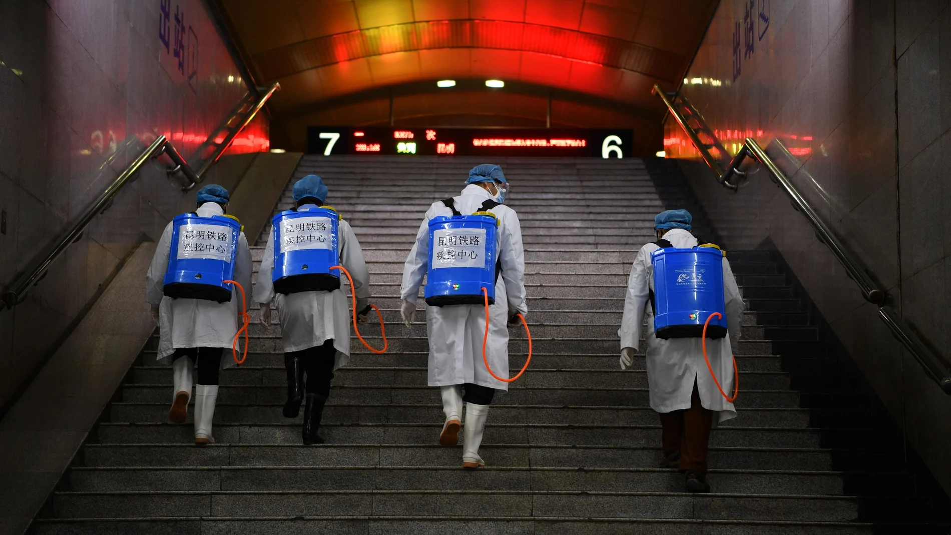 Workers with sanitizing equipment walk up a flight of stairs as they disinfect a railway station in Kunming