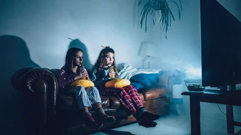 Jóvenes viendo la televisión en el sofá de su casa mientras beben zumo