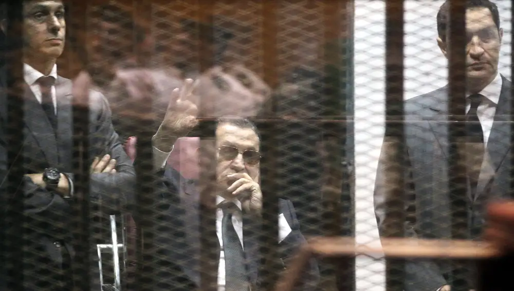 Hosni Mubarak, flanqueado por sus hijos, saluda desde la celda desde la que escuchó el veredicto contra él.