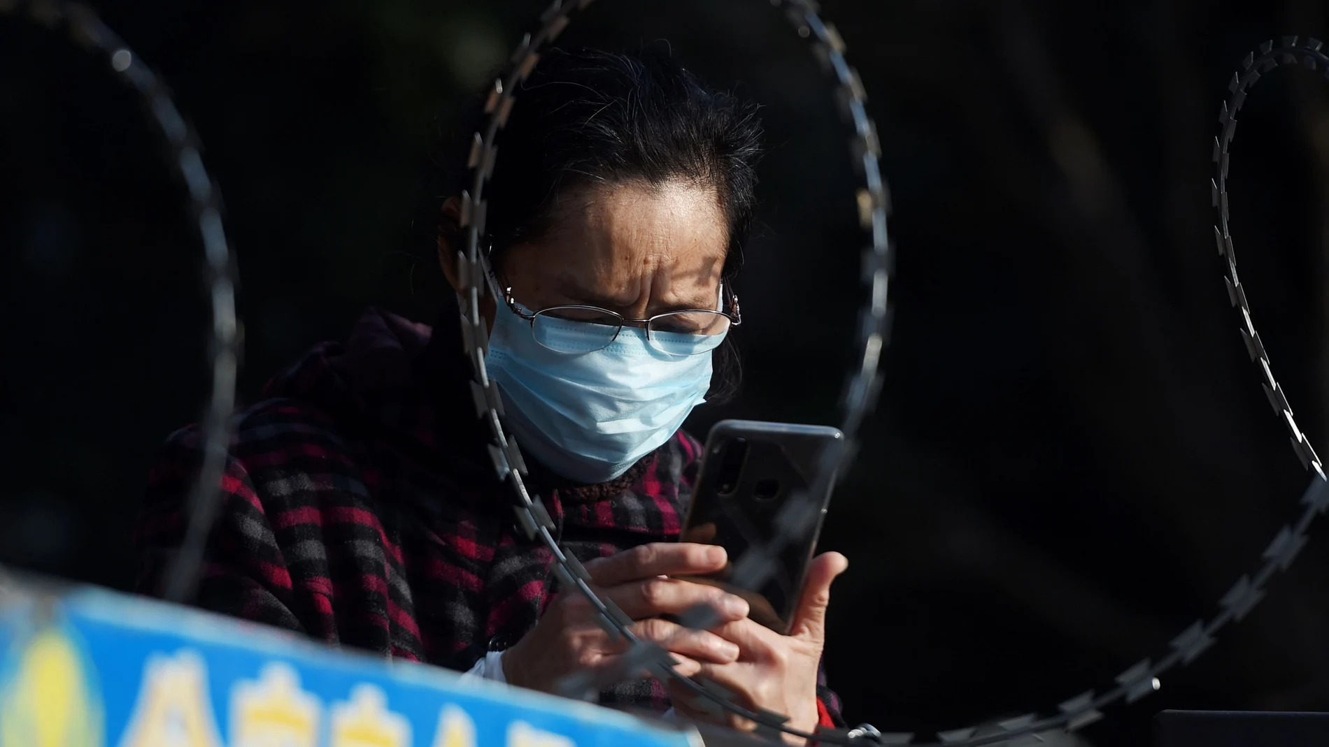 FILE PHOTO: A woman uses her mobile phone behind barbed wire at an entrance of a residential compound in Wuhan