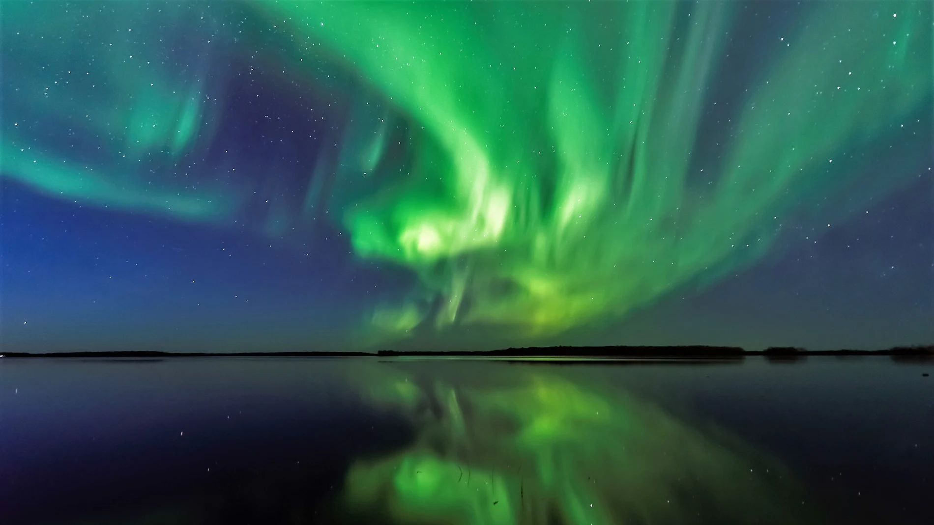 Imagen de una aurora boreal en el cielo y reflejada en la superficie de un lago