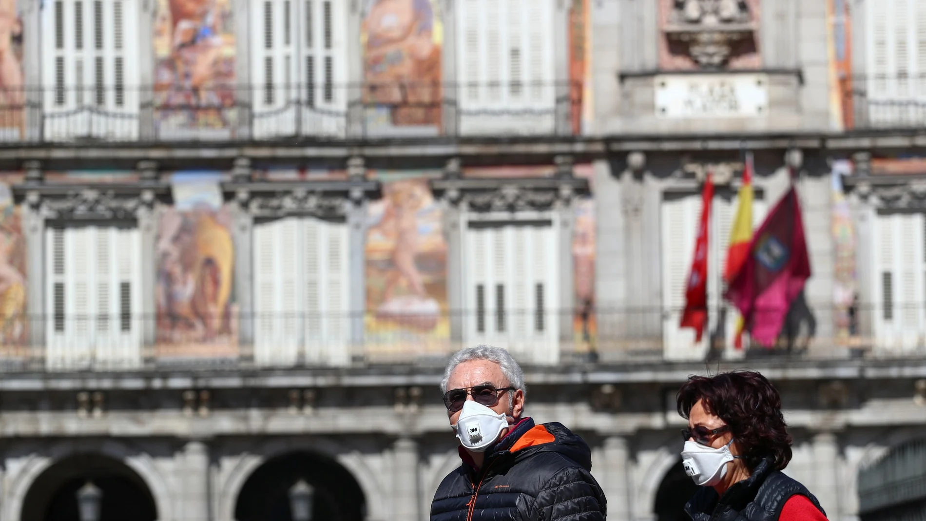 A couple wear protective face masks as they walk at one of the main touristic landmarks Plaza Mayor in Madrid